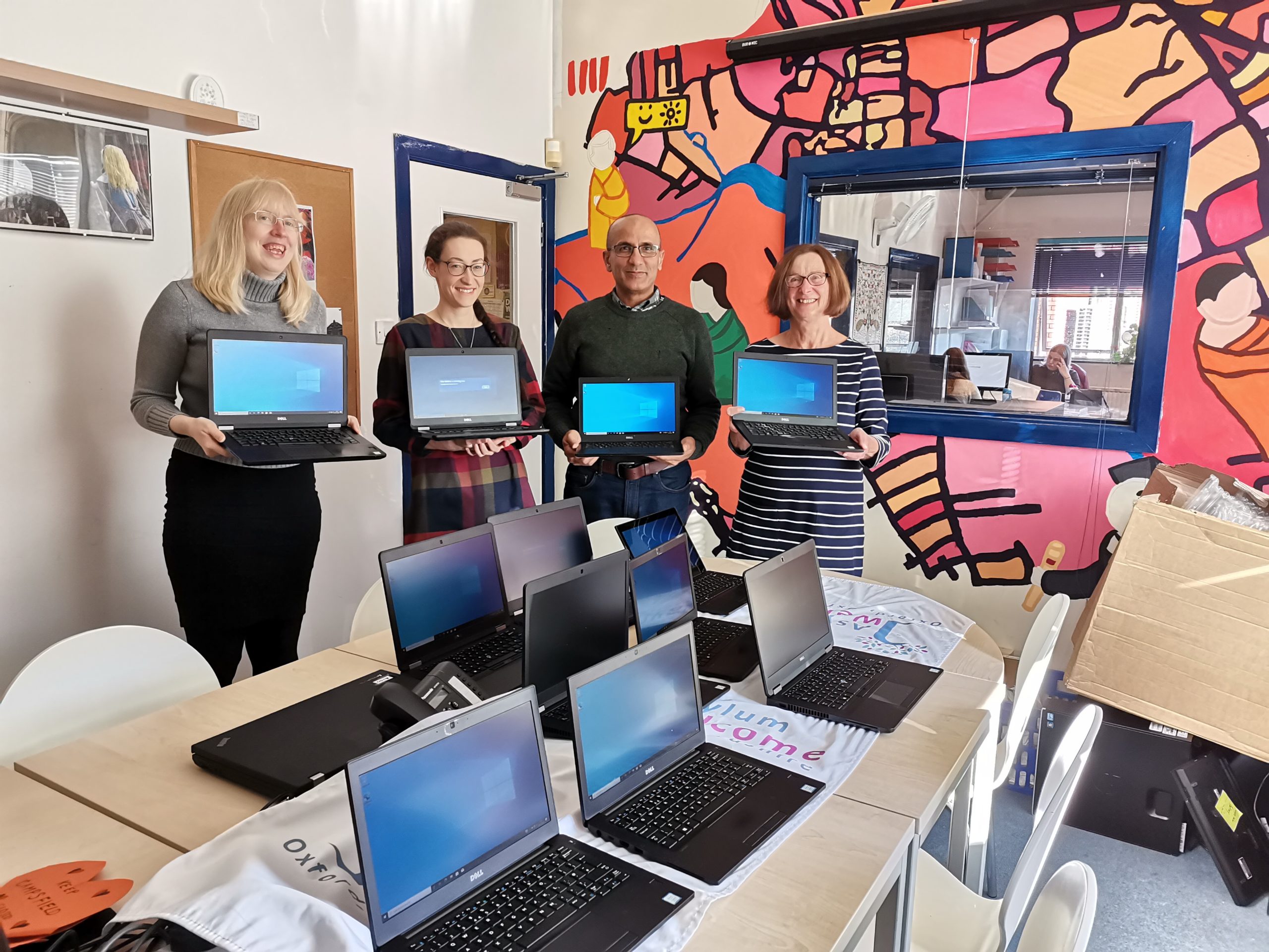 Asylum Welcome staff holding donated laptops. More laptops can be seen on the table.