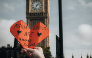 Orange heart held up in front of St Stephen's Tower (Big Ben). Message on heart reads "Asylum Rights Are Human Rights".