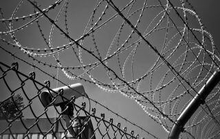 Close-up black-and-white image of barbed wire and a security camera